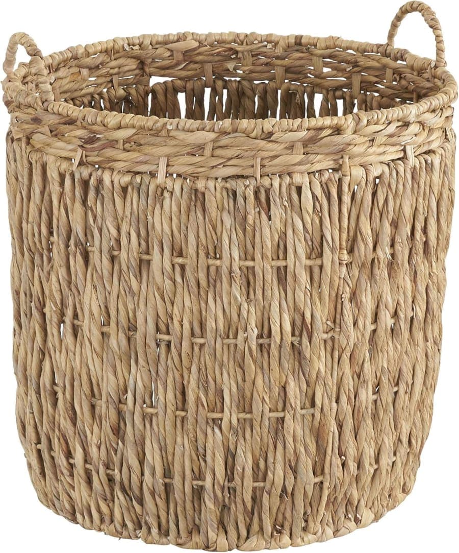 Tall natural woven wicker basket with handles, handmade rustic floor storage for laundry and blankets in a living room.