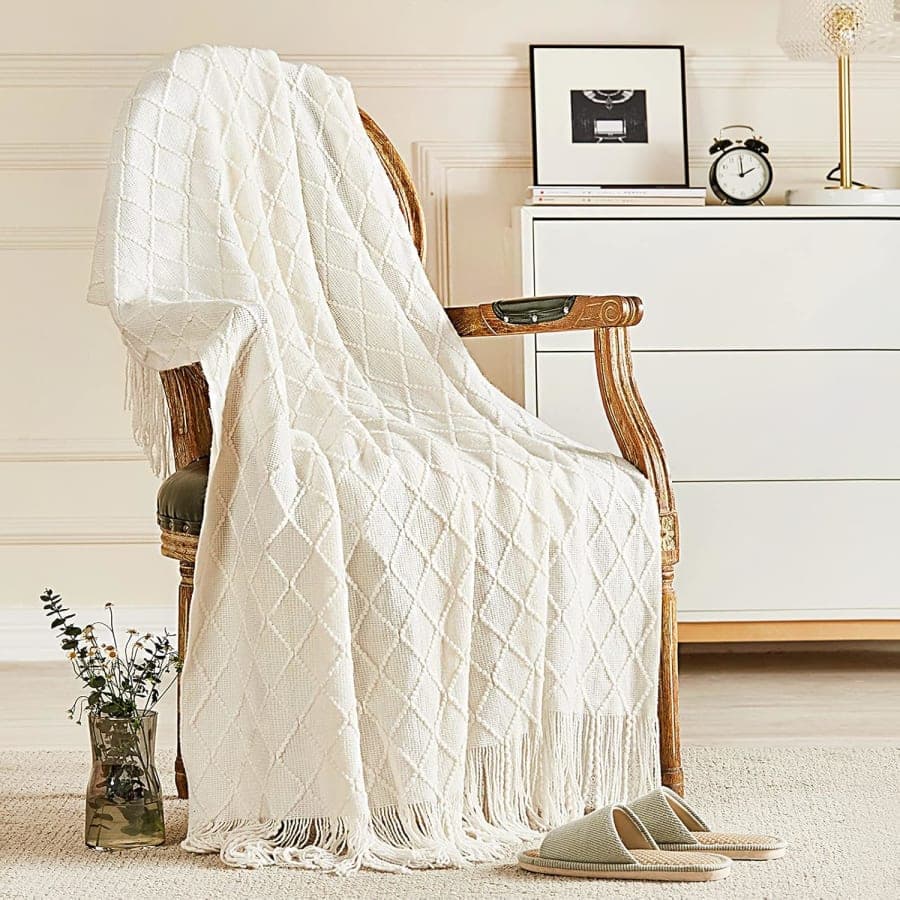 Ivory knitted throw blanket with tassels draped over a chair for cozy farmhouse home decor