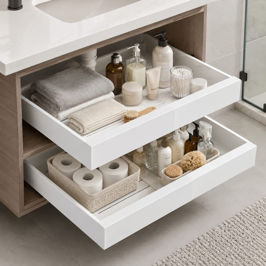 White pull-out bathroom vanity drawers organized with folded towels, toiletries, cotton swabs, toilet paper, and bath essentials.