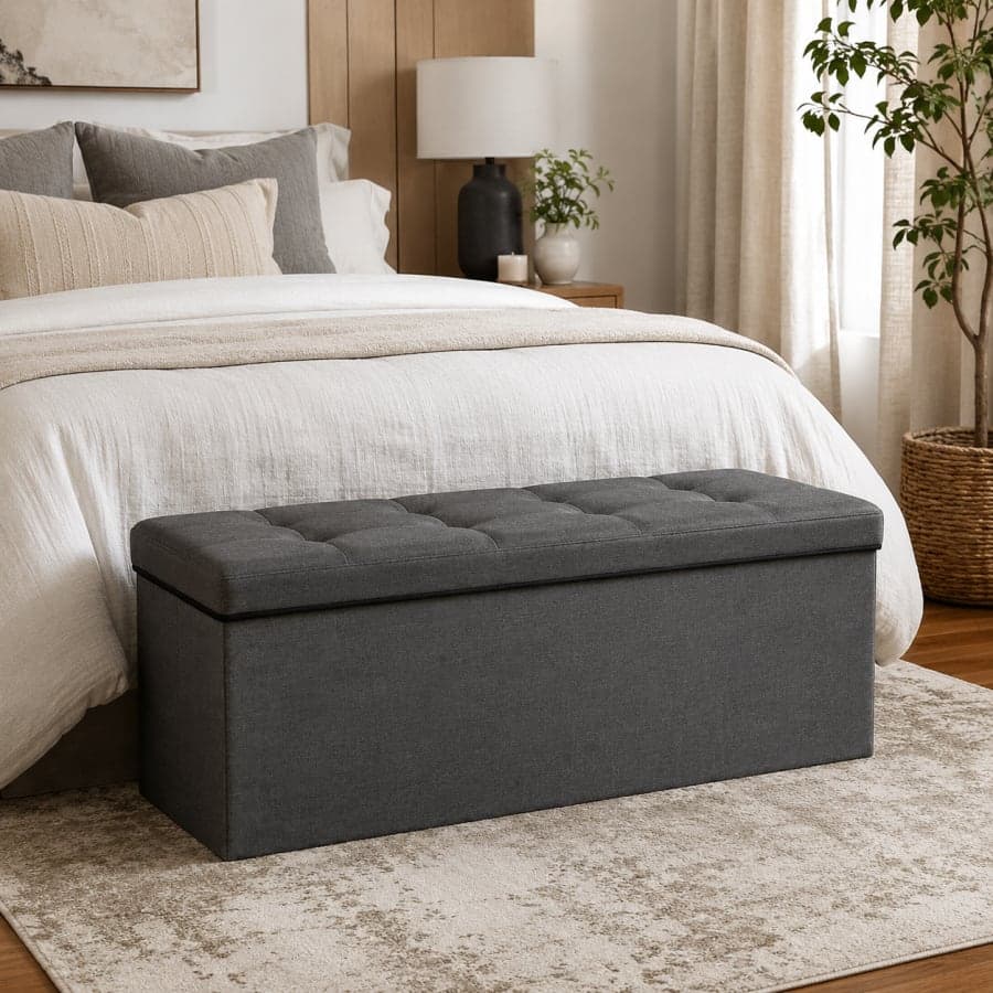 Dark gray storage ottoman bench placed at the foot of a neatly styled neutral bedroom bed with soft natural light.