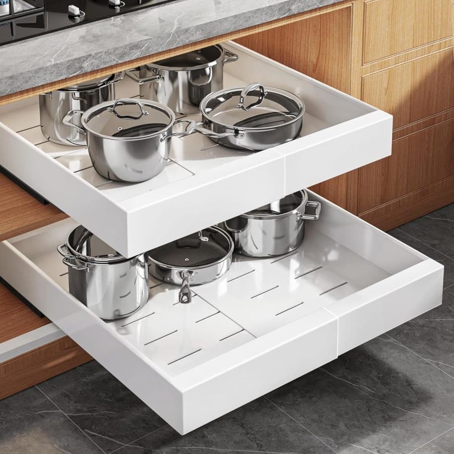 White pull-out cabinet organizer drawers holding stainless steel pots and pans inside a wood kitchen cabinet.
